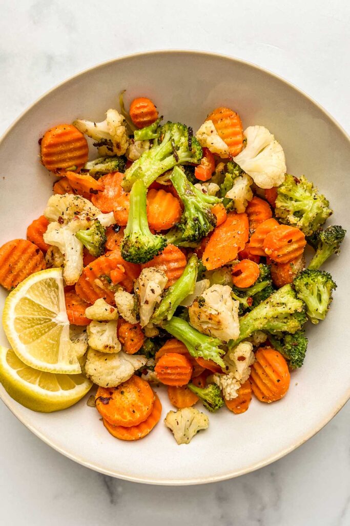 Roasted California mix vegetables in a white serving bowl with two slices of lemon.