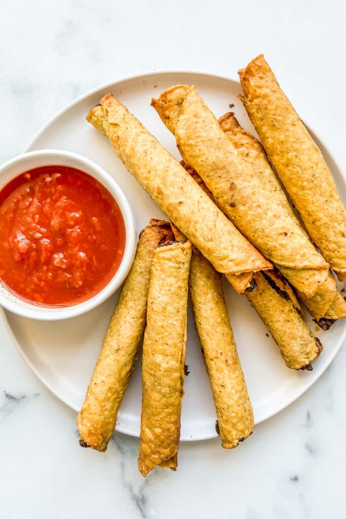 Air fried taquitos on a plate with a bowl of salsa.