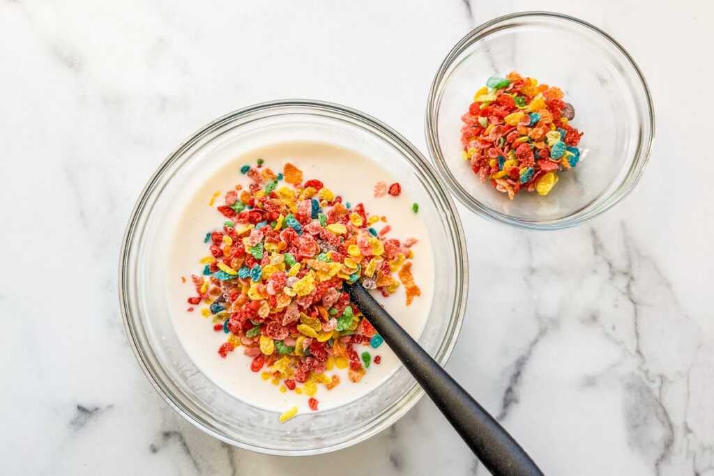 Fruity Pebbles cereal being mixed into a bowl of yogurt and milk.