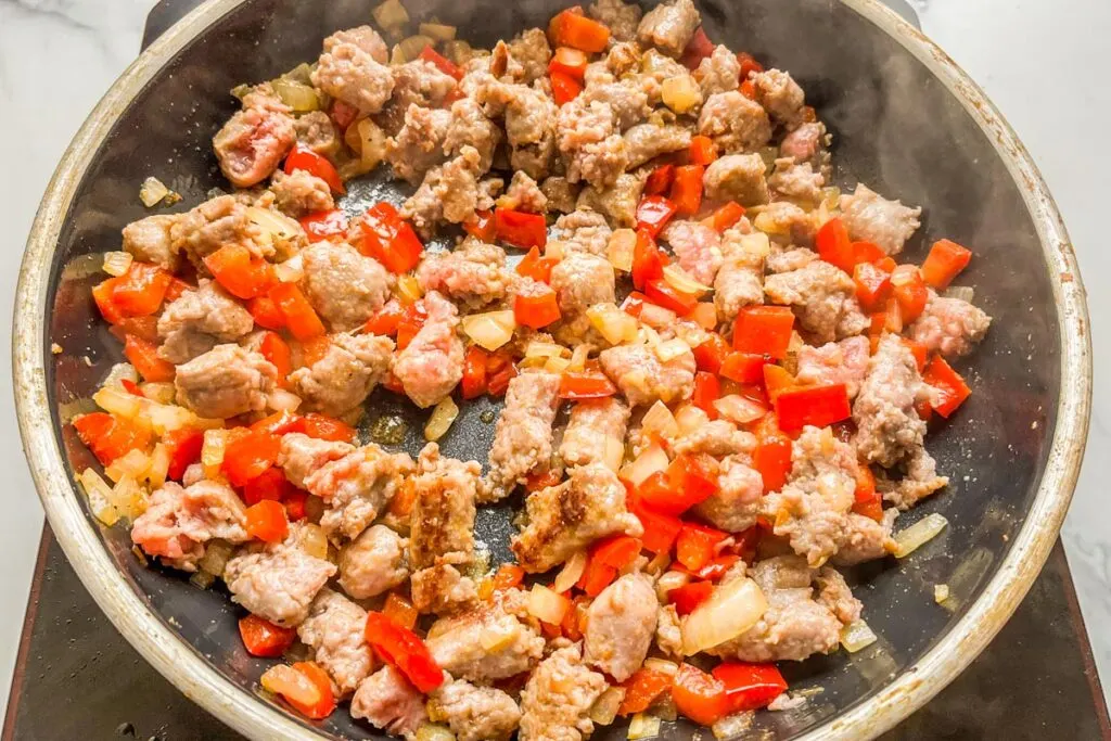 Cooking sausage, bell peppers, and onions in a frying pan.