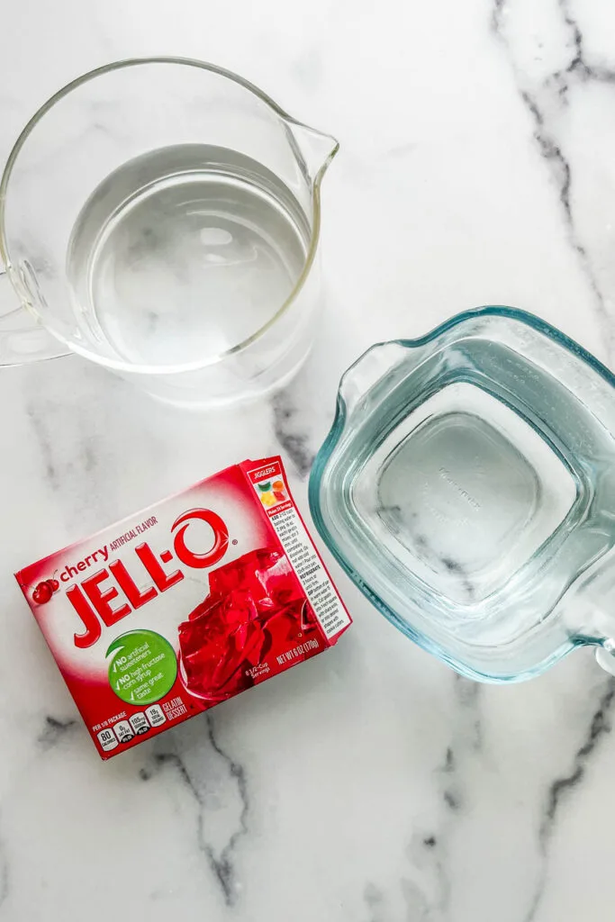 Two containers of water and a box of cherry jello mix.