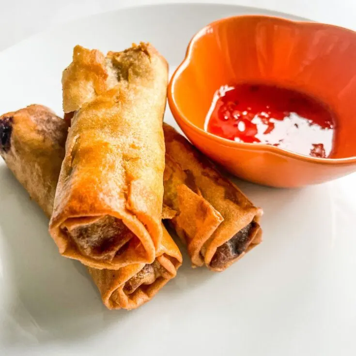 Cooked Vegetable Egg Rolls on plate next to dip of sweet chilli sauce